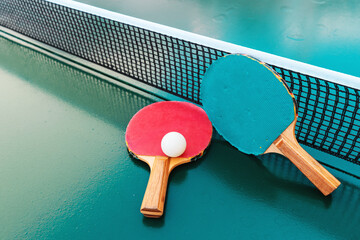 Table tennis rackets and ping-pong balls on green table surface with net