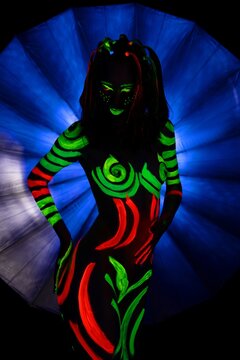 Anonymous woman with neon body paints in dark room