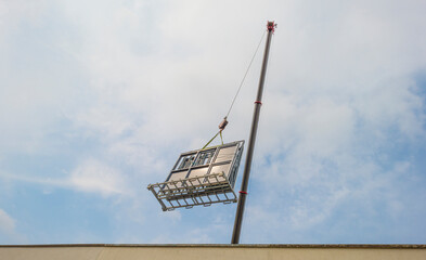 Crane hoisting building material for renovation over the flat roof of a house under a blue cloudy...