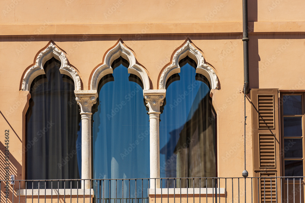 Wall mural Close-up of three ancient windows with arch in Venetian Gothic style and stone architectural columns with capitals. Brescia downtown, Cathedral square, Lombardy, Italy, Europe.