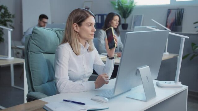 Footage of female company employee consulting client on phone. Shooting of young blonde businesswoman sitting on comfortable designer chair, talking on mobile. Woman using computer and cellphone