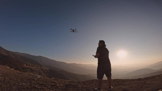 Young man takes off drone from his hand to work with videos and photos. Modern entertainment for future generation. Silhouette of man in sunset. Enjoy the technology in the midst of natural landscapes