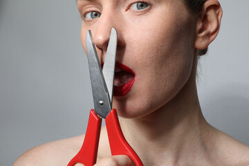 Close-up of young woman with scissors looking at the camera posing on white wall