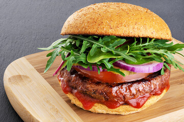 Burger with vegan meat patty on cutting board background.