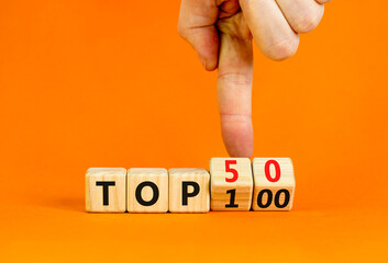From Top 100 to 50 symbol. Businessman turns wooden cubes and changes concept words Top 100 to Top 50. Beautiful orange table and background. Business and from Top 100 to Top 50 concept. Copy space.