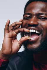 A man with dark skin is presenting holding a ice cube. He is wearing a black leather jacket and a red golf or shirt. He is holding a cube near his mouth in his right hand.
