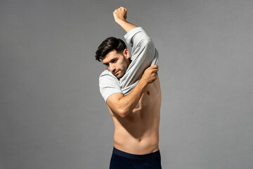 Beard caucasian man putting on t-shirt while standing on gray isolated background in studio