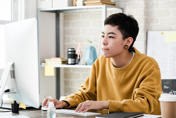 Young Asian tomboy woman in casual attire looking at computer while working from home
