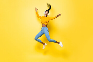 Full body portrait of happy African American woman listening to music and jumping with hands...