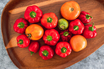 freshly picked mini capsicums and tomatoes with vibrant red and orange tones on wooden tray, simple ingredients concept