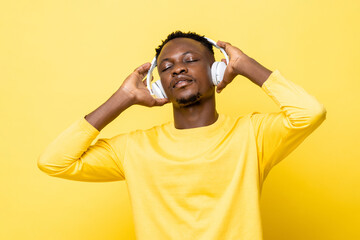 Portrait of young African man listening to music closing eyes and holding headphones against yellow...