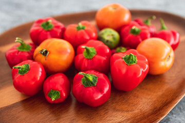 freshly picked mini capsicums and tomatoes with vibrant red and orange tones on wooden tray, simple ingredients concept