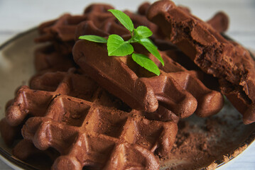 Delicious Belgian chocolate waffles on a ceramic plate on a light wooden countertop.