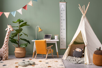 Creative composition of stylish and cozy child room interior design with green wall, plush toys, bright carpet, armchair, stool and accessories. Desk with lamp and computer plush toys. Template.