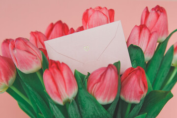 pink paper envelope with a heart in a bright spring bouquet of pink tulips, the concept of romance, gift and holiday greetings