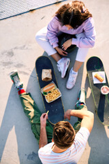 Top view on teenagers eating fast food on their skateboards. Selective focus on a teenage boy's head who sits with his female friend. © chika_milan