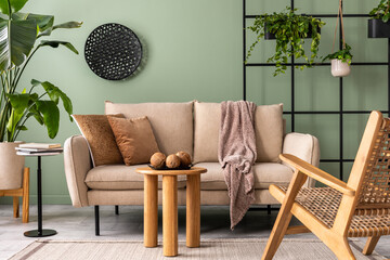 The stylish composition at living room interior with design beige sofa, coffee table, rattan armchair, plants and elegant personal accessories. Brown pillow and plaid. Cozy apartment. Home decor.