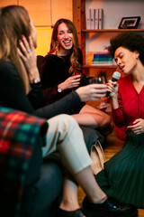 A multicultural group of female friends sings karaoke while drinking alcohol in the living room.