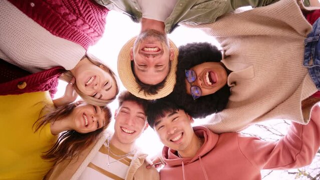 Low angle of group of cheerful young friends in circle taking selfie portrait. Happy people looking at the camera smiling. Concept of community, youth lifestyle and friendship