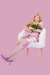 young woman with flowers sits on a white chair on a pink background