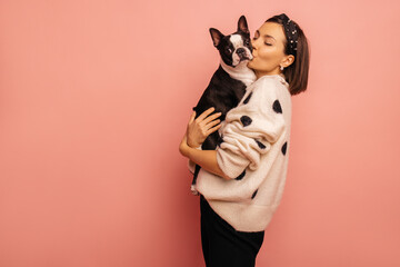 Beautiful young caucasian woman kissing her cute dog on pink background with space for text....
