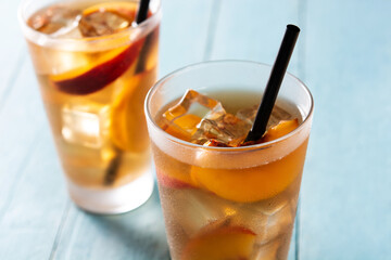 Glass of peach tea with ice cubes on blue wooden table