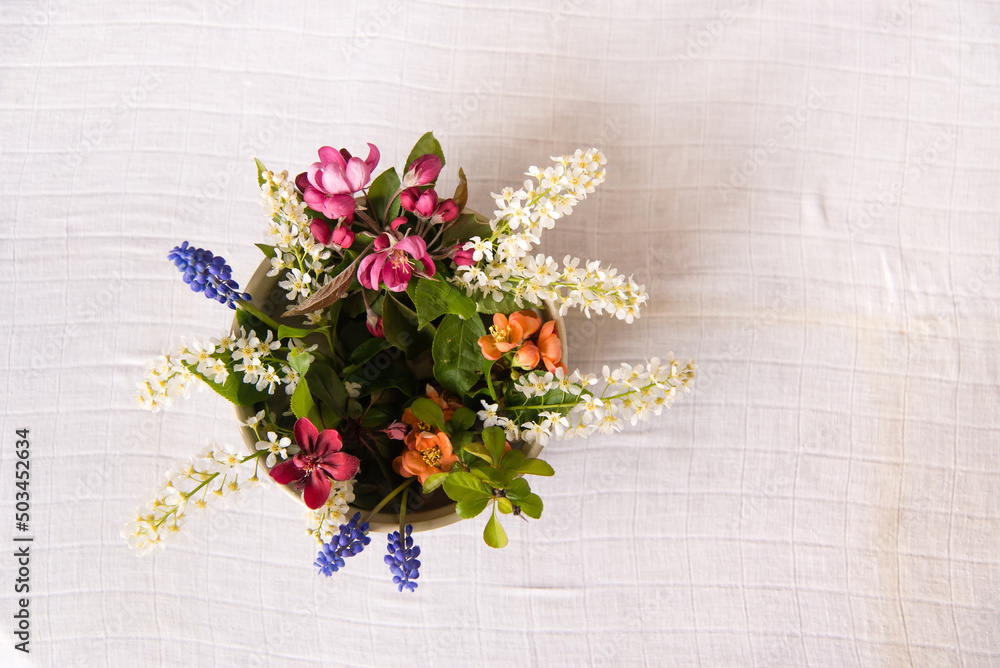 Wall mural Spring blooming delicate flowers in a round vase on a table with a white tablecloth, a pastel bouquet and a delicate floral card