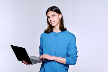 Teenage male student using laptop posing looking at camera on light studio background