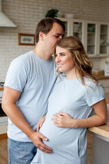 Fototapeta premium pregnant woman and her handsome husband embracing and smiling while spending time together near window at home. Romantic couple expecting new baby indoors. Parenthood concept