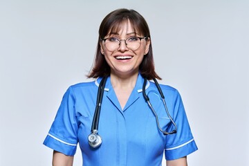 Headshot portrait of nurse in blue uniform looking at camera on light studio background