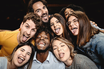Portrait of happy friends embracing and making grimaces tongue out looking at the camera - people...