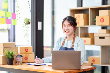 Startup small business entrepreneur or freelance Asian woman using a laptop with box, Young success Asian woman with her hand lift up, online marketing packaging box and delivery, SME concept.