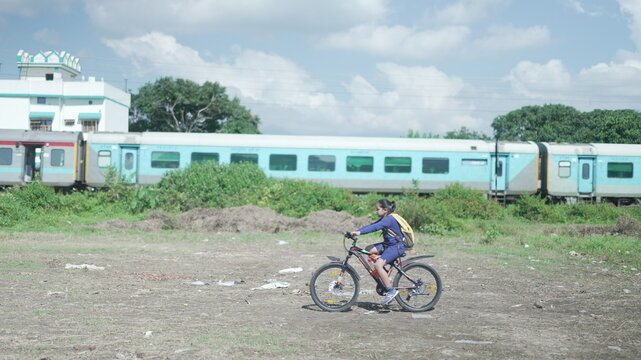 An Indian Kid cycling on a road, near a sugarcane field in a rural area of Uttarakhand, India. Indian train passing from the background. Physical fitness of an Indian boy. High-quality image.