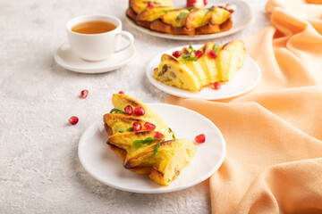 Cheesecake with cup of tea on gray concrete background and orange textile, side view, close up.