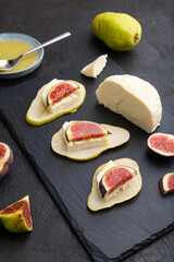 Summer appetizer with pear, cottage cheese, figs and honey on a black concrete background. Side view.