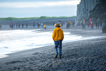 People walking on the beach. Waves of the Atlantic ocean fall on the black sand of the beach of...