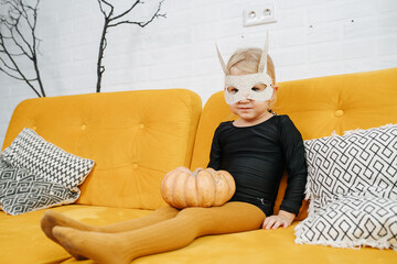 Chubby little girl in a mask dressed for halloween on a couch, grimacing