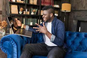 Happy young male black freelancer talking on conference video call to colleagues online. Afro American student talking to teacher and other students on laptop at home. Online meeting, lesson