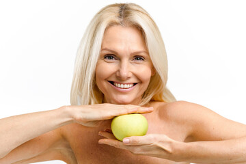 Happy senior woman holding fresh green apple middle her hands and smiling. Elderly model with naked shoulders posing and looking at the camera isolated on white. Anti age treatment