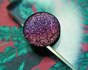 Single glittery violet eye shadow on floral leaf background with acrylic