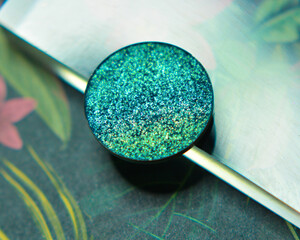 Single glittery turquiose eye shadow on floral background with acrylic and hint of light - obrazy, fototapety, plakaty