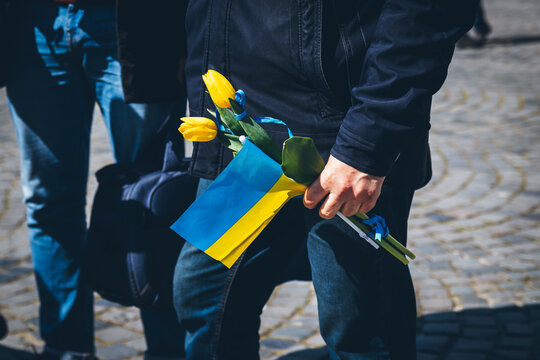 In the man's hand is a Ukrainian flag and flowers to honor the dead peaceful Ukrainians. 