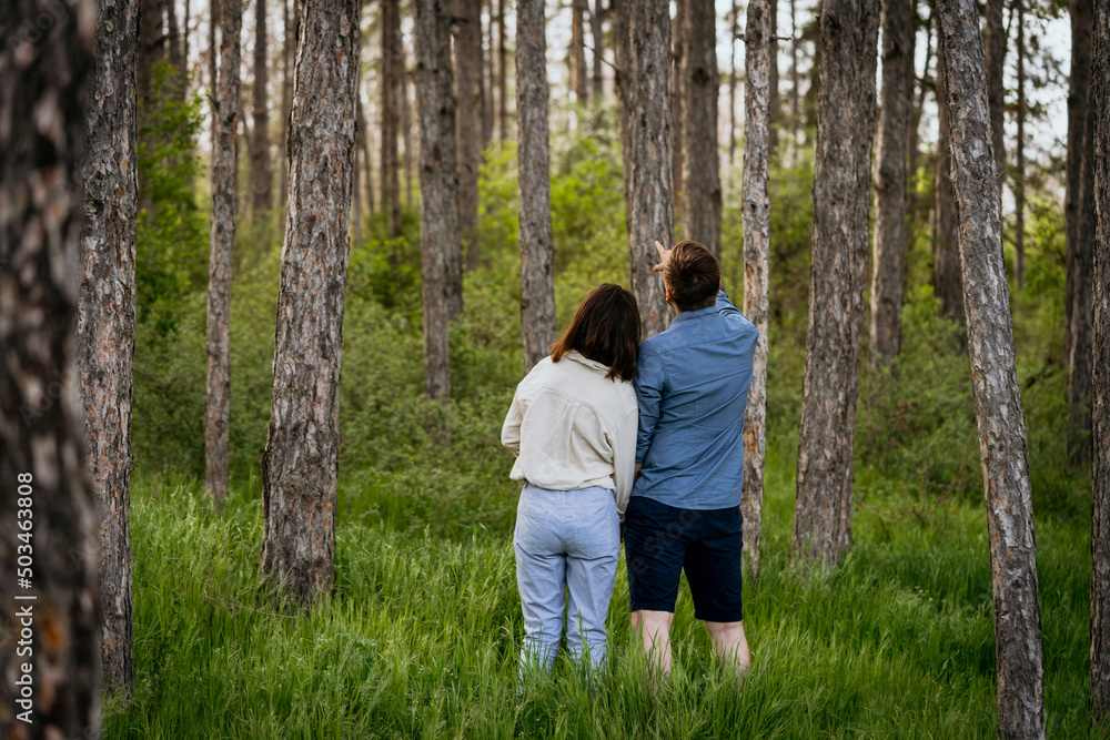 Wall mural Young couple standing together in forest, with man pointing up. Man and woman looking at something interesting in the forest.