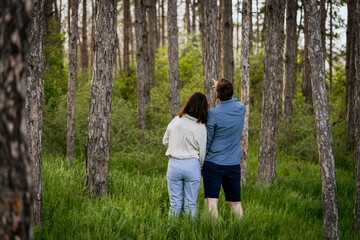 Young couple standing together in forest, with man pointing up. Man and woman looking at something interesting in the forest.