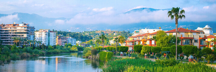 Beautiful river embankment with park area against backdrop of picturesque mountains in city of...