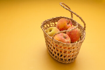 Group of fresh peaches fruits in a basket over a yellow background