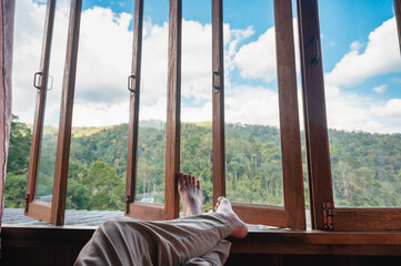 Barefoot man legs relaxing by wooden window in the bedroom and mountain view in countryside