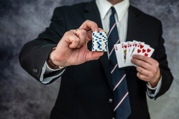 Stylish man in black suit holding play cards and poker chips in casino