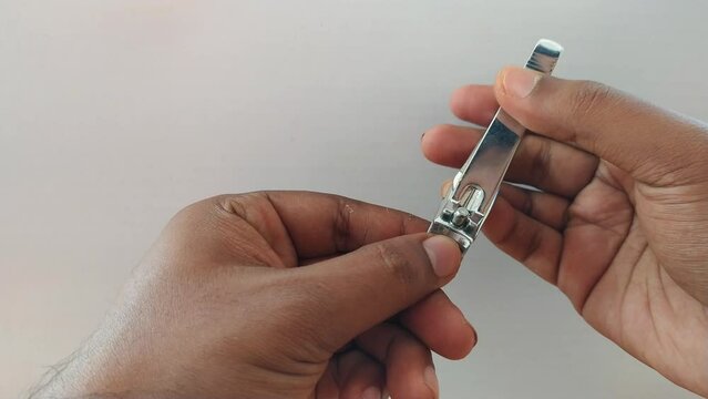 Adult woman or man self care grooming, cutting or trimming unpainted healthy fingernail using traditional stainless steel nail cutter tool with white background. Beautiful close up macro side view.