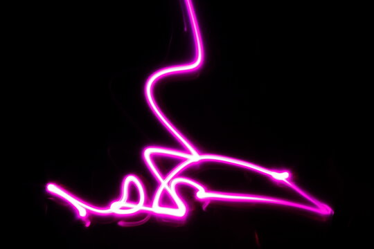 Las l&iacute;neas de luz hal&oacute;gena de color rosa describen una figura de garabatos con curvas en el espacio formando un hermoso dise&ntilde;o abstracto con un fondo negro